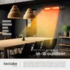 A modern dining room with a long wooden table and chairs, illuminated by a wall-mounted infrared heater casting a warm glow. Náhled obrázku produktu