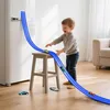 A young boy plays with a blue toy car race track set attached to a wall and supported by a stool. Produktbild-Vorschau