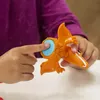 A child's hands are shown interacting with an orange dinosaur toy. Náhled obrázku produktu