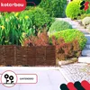 A garden scene with a woven willow fence in the foreground and lush greenery in the background. Anteprima dell’immagine prodotto