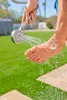 A person is rinsing their foot with a handheld shower head outdoors on a sunny day. Produktbild-Vorschau