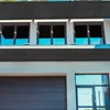 A modern building facade with a garage door and windows, partially obscured by a dark fabric screen. Produktbild-Vorschau