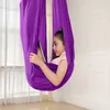 A young girl is sitting in a purple aerial hammock, looking at a tablet. Voir les images du produit