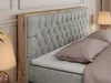 A close-up view of a bed with a tufted headboard and wooden frame. Produktbild-Vorschau