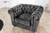 A gray velvet armchair with button tufting sits on a wooden floor in a room. Produktbild-Vorschau