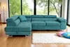 A teal sectional sofa is placed in a living room with large windows overlooking a lush green landscape. A white rug and colorful pillows are in front of the sofa. Produktbild-Vorschau