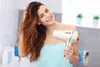 A woman in a bathroom is drying her hair with a white hairdryer. Anteprima dell’immagine prodotto