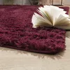A close-up of a plush, burgundy rug with an open book resting on it, placed on a light wooden floor. Produktbild-Vorschau