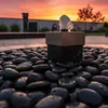 Schwarze polierte Flusskiesel um eine Gartenbeleuchtung bei Sonnenuntergang Produktbild-Vorschau