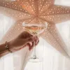 A hand holding a glass of champagne in front of a star-shaped light. Produktbild-Vorschau