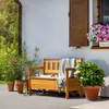 A wooden garden bench with storage is placed on a patio next to potted plants and flowers. Náhled obrázku produktu