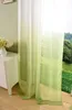 A close-up view of a sheer curtain with a green gradient, partially covering a window with a view of trees and grass. Produktbild-Vorschau