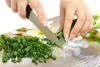 Hands chopping green onions on a cutting board with a floral pattern. Náhľad obrázku produktu