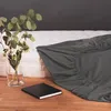 A dark gray fitted sheet is laid out on a white mattress, with a vase of eucalyptus and white flowers to the left and a black notebook on the wooden floor in the foreground. Anteprima dell’immagine prodotto