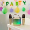 A karaoke set with two microphones and a speaker is displayed on a table in front of a party decoration. Anteprima dell’immagine prodotto