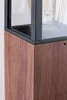A close-up view of the corner of a modern outdoor lamp, showing the wood-grain texture of the base and the black metal frame surrounding a glass enclosure with a light bulb inside. Podgląd zdjęcia produktu