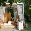 An outdoor patio scene with a white gas patio heater as the main focus, surrounded by wicker furniture, decorative screens, and dried plants. Produktbild-Vorschau
