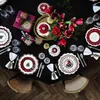 A beautifully set dining table for a Christmas meal, featuring festive plates, cutlery, napkins, gifts, and a bouquet of red flowers. Podgląd zdjęcia produktu