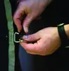 A close-up shot of hands connecting a buckle and clip to a tan strap. Produktbild-Vorschau