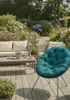A comfortable outdoor seating area with a sofa, coffee table, and a round cushion chair, surrounded by lush garden greenery and flowers. Produktbild-Vorschau