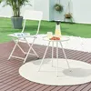 A white folding chair and a small white side table with a pitcher of lemonade and strawberries are set up on a wooden deck in a backyard setting. Náhled obrázku produktu