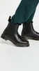 A pair of black Dr. Martens Chelsea boots with fur trim, worn with dark green sweatpants. Produktbild-Vorschau