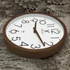 A wooden wall clock with a white face and brown hands is placed on a textured, rough surface that resembles wood or bark. Voir les images du produit