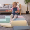 A young child sits on soft play blocks in a living room setting. Produktbild-Vorschau