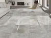 A modern living room with a tiled floor, a sofa, a fireplace, and a chair. A square metal frame is visible on the floor. Produktbild-Vorschau