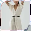 A woman wearing a beige dress cinched with a black belt. Náhled obrázku produktu