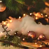 Close-up of Christmas lights and ornaments on a wooden surface with pine branches and cotton batting. Produktbild-Vorschau