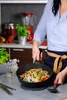 A person is cooking pasta with vegetables in a wok on a stovetop. Produktbild-Vorschau