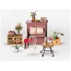 A miniature dollhouse scene featuring a piano, a small table with chairs, and a bookshelf. Anteprima dell’immagine prodotto