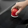 A hand is holding a red and white polishing tool on a black surface, creating circular marks. Podgląd zdjęcia produktu