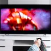 A hand holding a remote control is pointed towards a television screen displaying a colorful, abstract image. Voir les images du produit