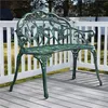 A green metal garden bench with a rose pattern sits on a wooden deck. Podgląd zdjęcia produktu