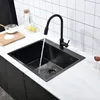 A black kitchen sink with water running from a black faucet, on a white countertop with a tiled backsplash. Produktbild-Vorschau