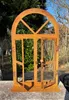 A rusty metal decorative window with open doors, placed outdoors on a stone surface with greenery and trees in the background. Produktbild-Vorschau