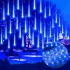 Blue meteor shower lights illuminate trees and a park at night, with buildings in the background. Produktbild-Vorschau