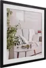 A framed picture of a living room scene with a sofa, plant, and coffee table. Produktbild-Vorschau