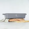 A gray baking dish with handles sits on a wooden board, partially covered by a linen cloth, with wheat stalks in the foreground. Náhled obrázku produktu