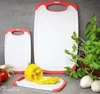 Two white cutting boards with red trim are shown on a gray surface, with a yellow pepper and other vegetables nearby. A plant is also visible. Anteprima dell’immagine prodotto