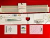 A knitting machine and its accessories are laid out on a red surface, with instruction manuals in the foreground. Produktbild-Vorschau
