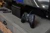 A black Nintendo Switch controller is placed on a gray dresser in front of a television. Anteprima dell’immagine prodotto