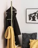 A corner of a room with a gold coat rack holding a black coat and a yellow scarf, next to a framed picture and two decorative pillows. Náhled obrázku produktu