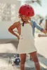 A young child wearing a red helmet and white overalls stands outdoors, looking down. Produktbild-Vorschau