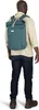 A man wearing a tan shirt and dark jeans stands with his back to the camera, wearing a teal Osprey Arcane Roll Top backpack. Produktbild-Vorschau