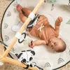 A baby is lying on a playmat with a gymini frame above them. Produktbild-Vorschau