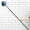 A hand holding a long-handled brush against a white tiled wall. Podgląd zdjęcia produktu