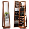 A jewelry cabinet with a full-length mirror is shown open, displaying its interior storage compartments filled with jewelry and cosmetics. The cabinet is made of wood and has a brown finish. The mirror reflects a potted plant and a window. Náhľad obrázku produktu